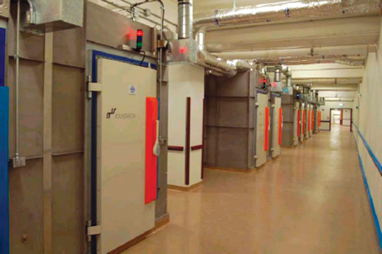 long hallway under fluorescent lights with multiple heavy doors along it