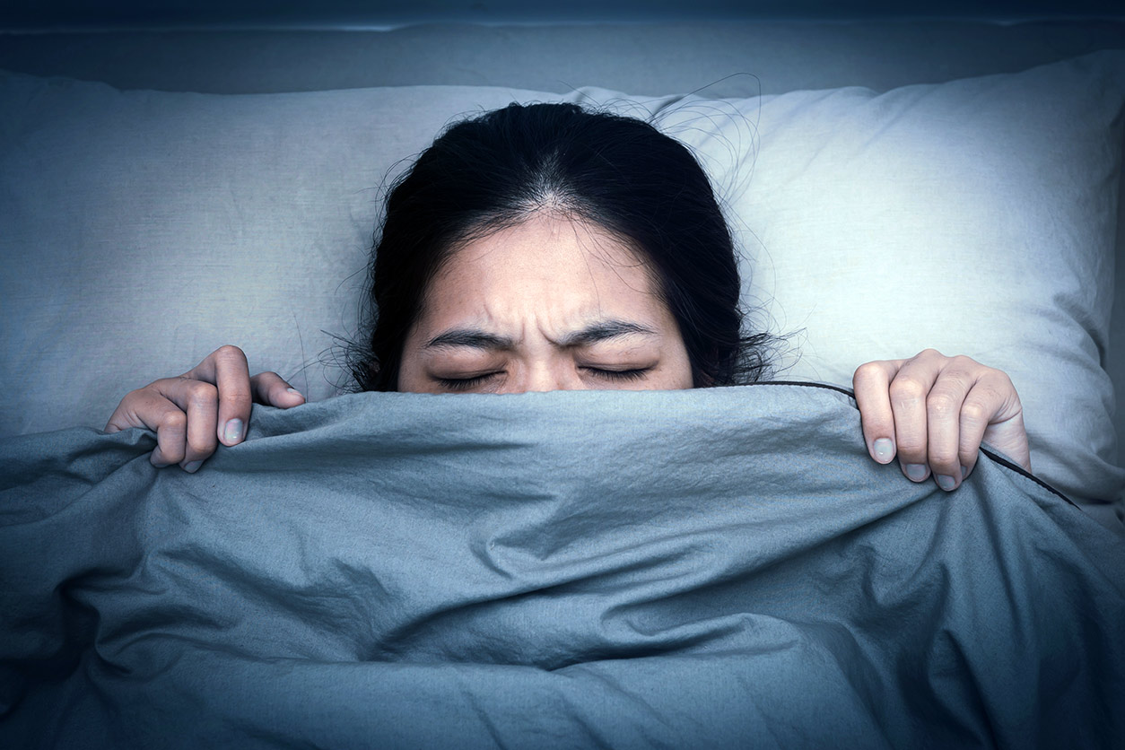 woman closing her eyes and holding blankets which cover her nose