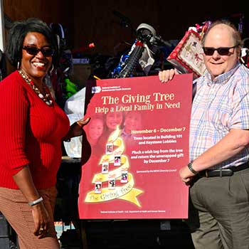 Volunteers holing the Giving Tree poster behind a truck filled with donated gifts