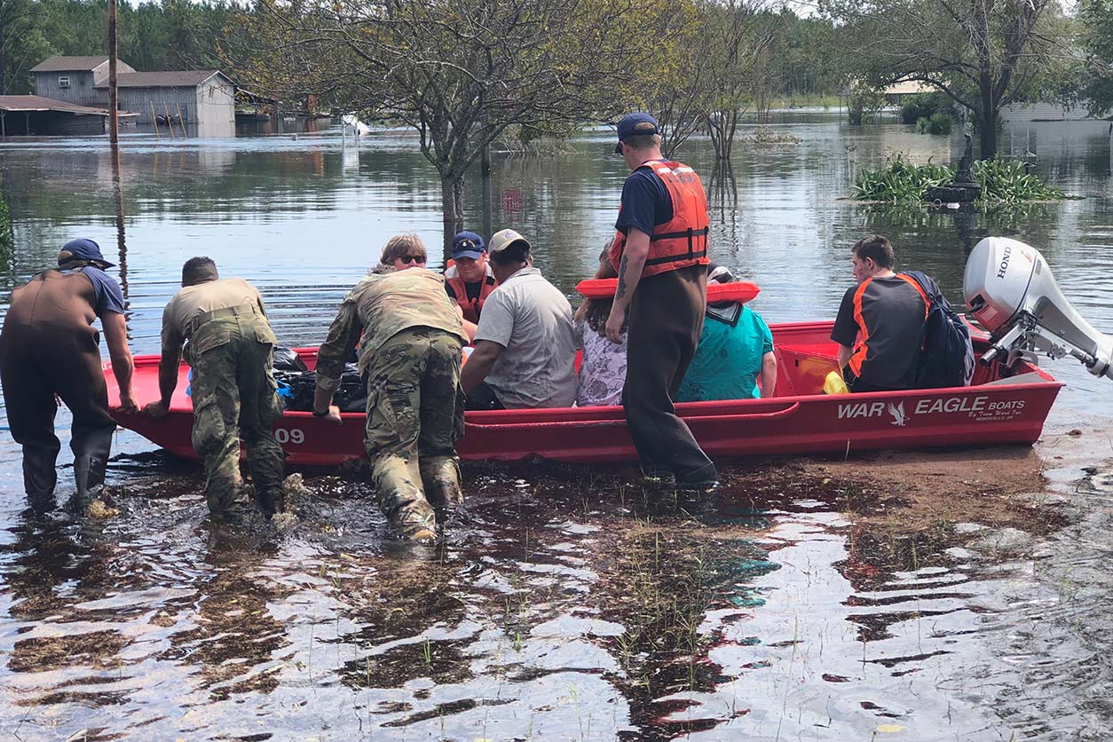 Members of the U.S. Coast Guard and North Carolina National Guard push a boat full of residents in flood waters.