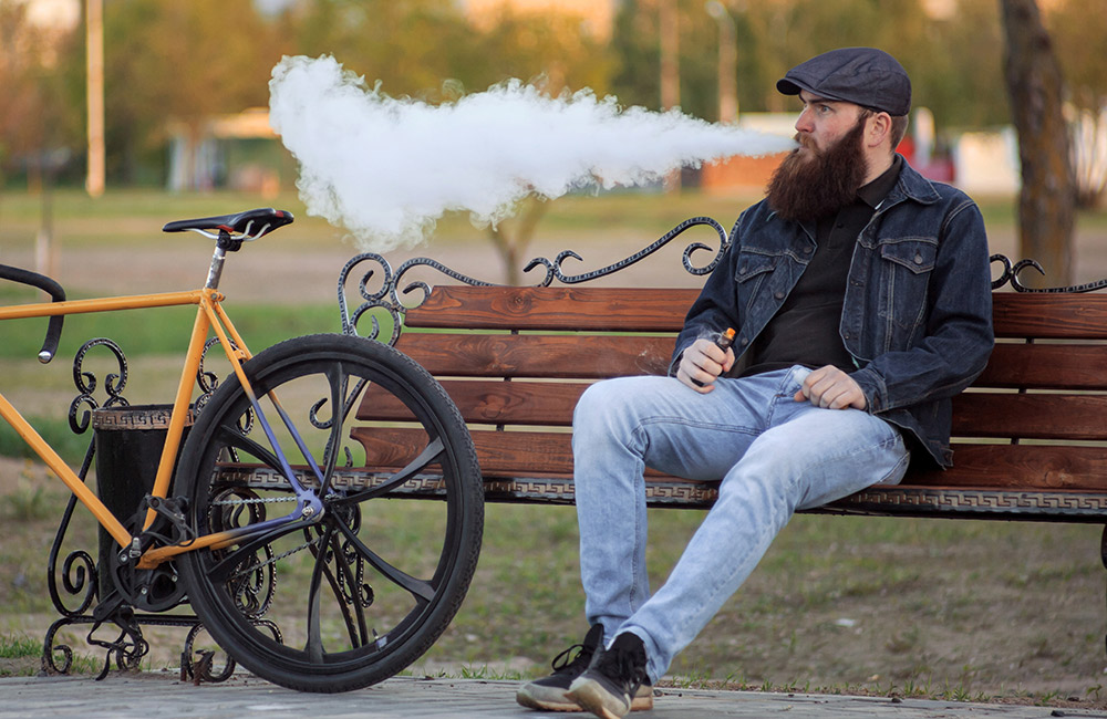 man sitting on bench next to a bicycle exhaling a large cloud of smoke