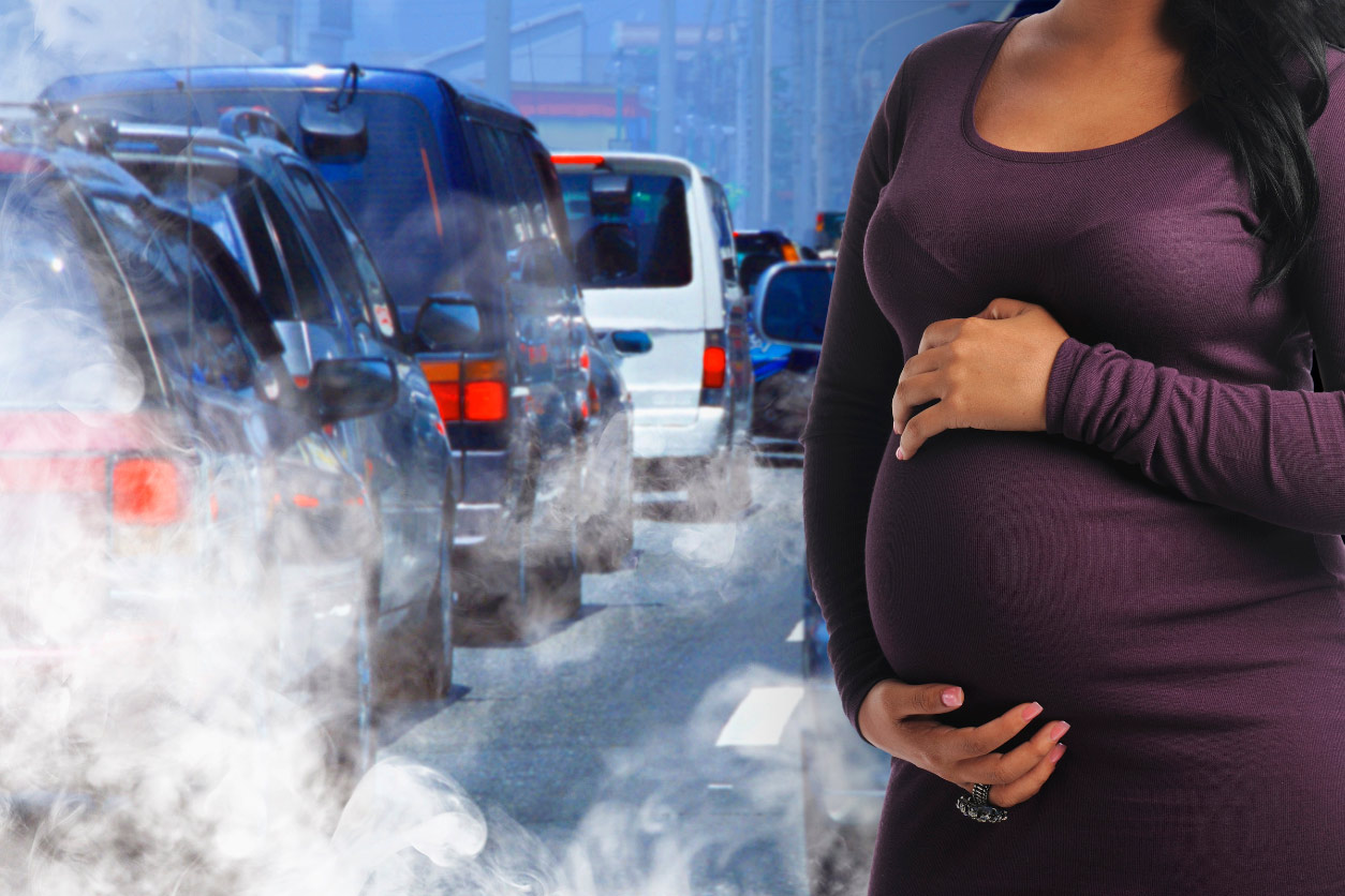 pregnant woman holding her rounded belly with traffic and combustion to her left