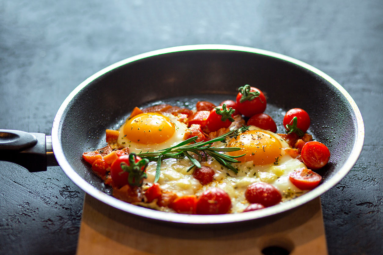 Fried scrambled eggs in a pan on a black background with cherry tomatoes, cheese and rosemary