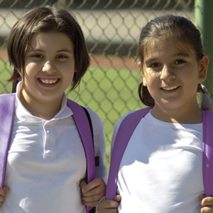 two girls smile while holding backpacks