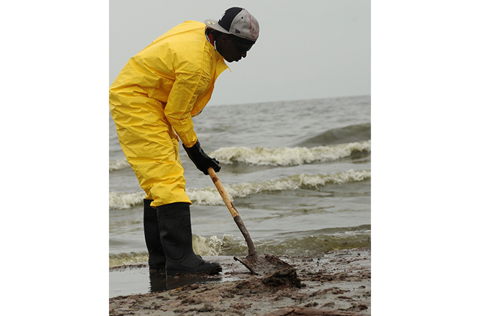 Worker shoveling layers of oil that washed ashore