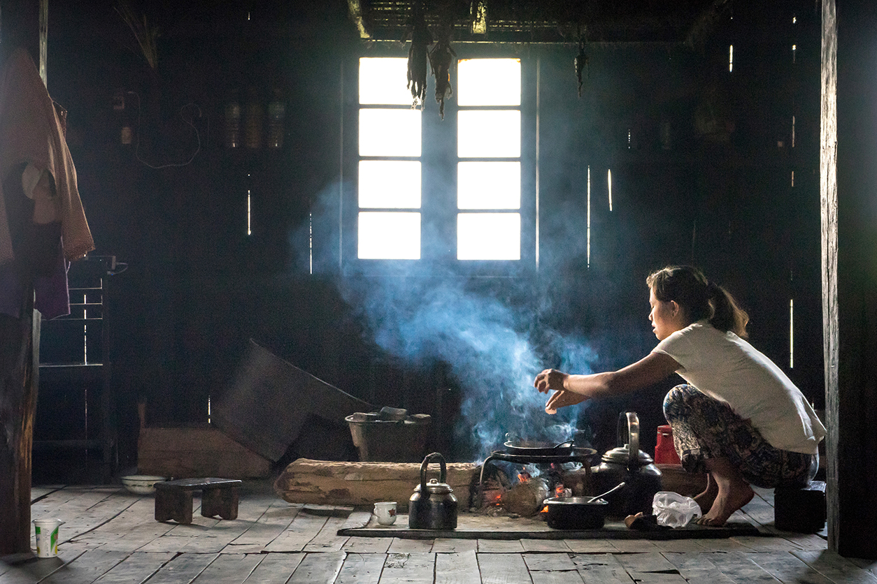 A woman cooks indoors on a makeshift cookstove