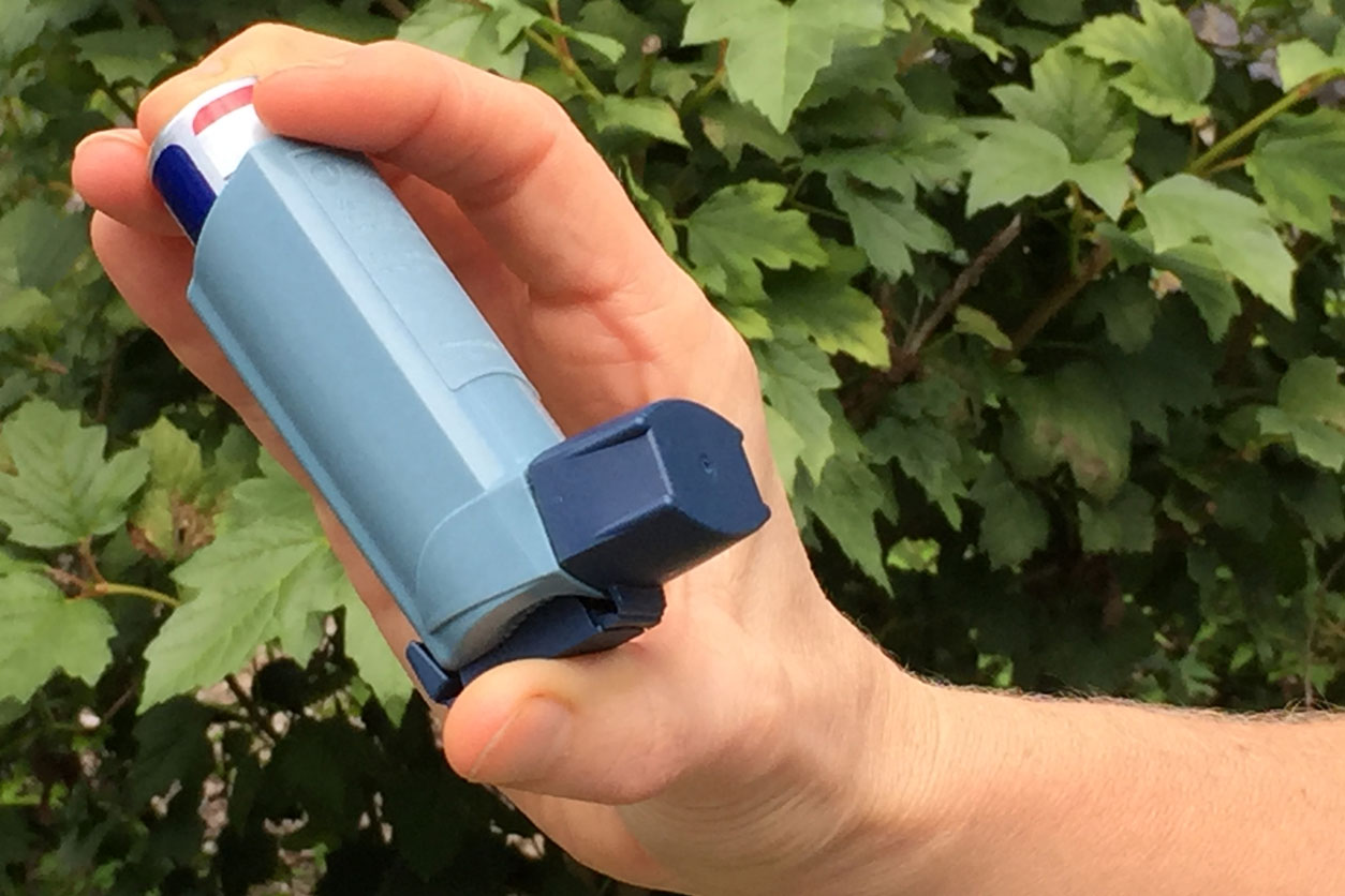 Hand holding blue asthma inhaler