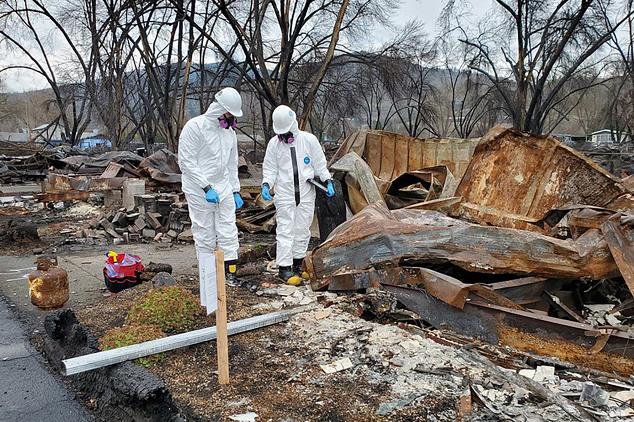 Two workers dressed in white safety uniforms during wildfire clenup in Almeda, Oregon.