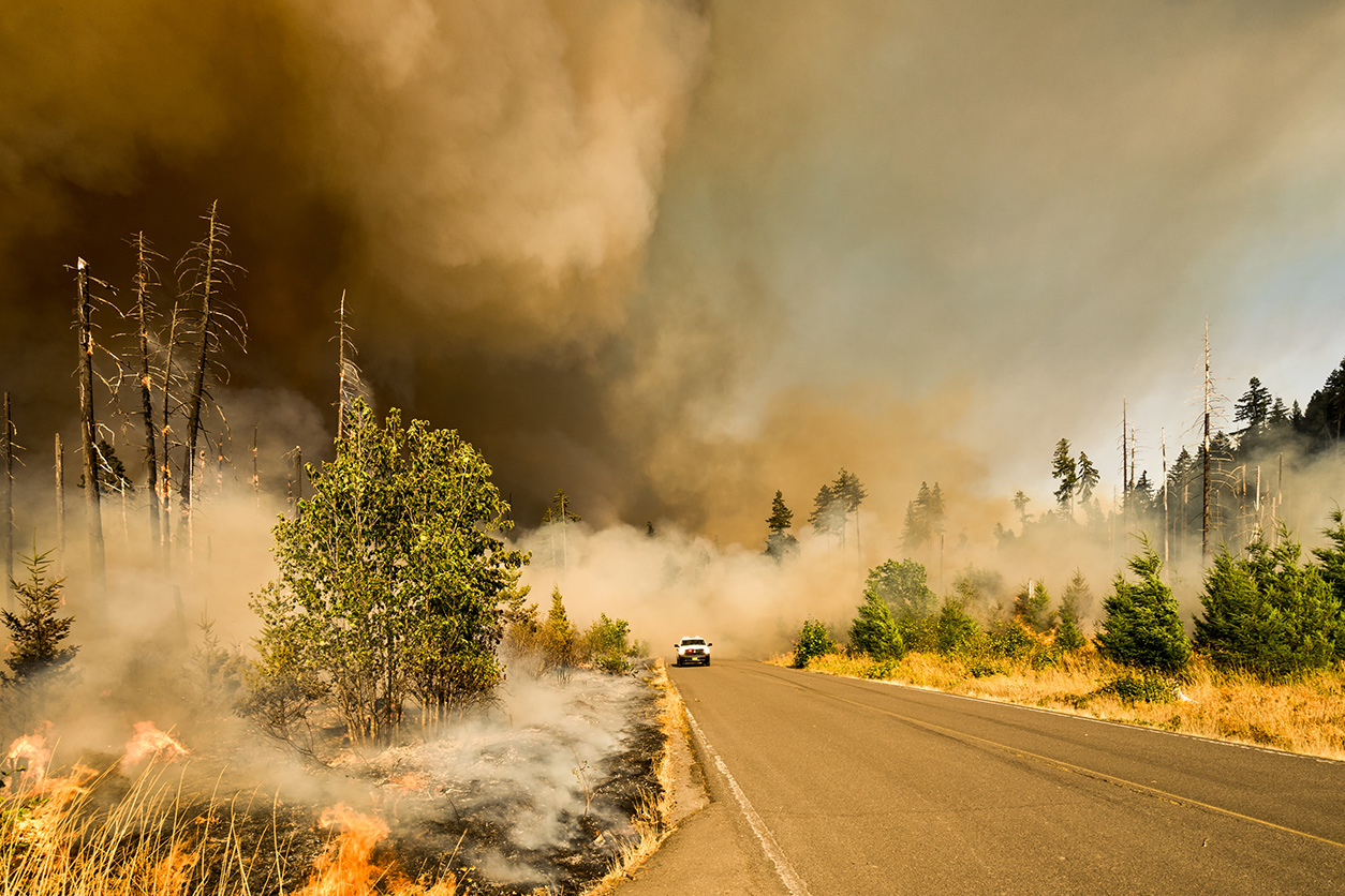 Car driving away from large wildfire