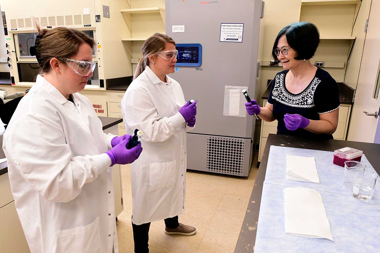 Huei-Chen Lee, Ph.D., right, explains pipetting, which is a technique used to measure and transfer liquids, to Chelsea Andrews, of Coastal Christian High School, Wilmington, and Ashley Haithcock, of Uwharrie Charter Academy, Asheboro.