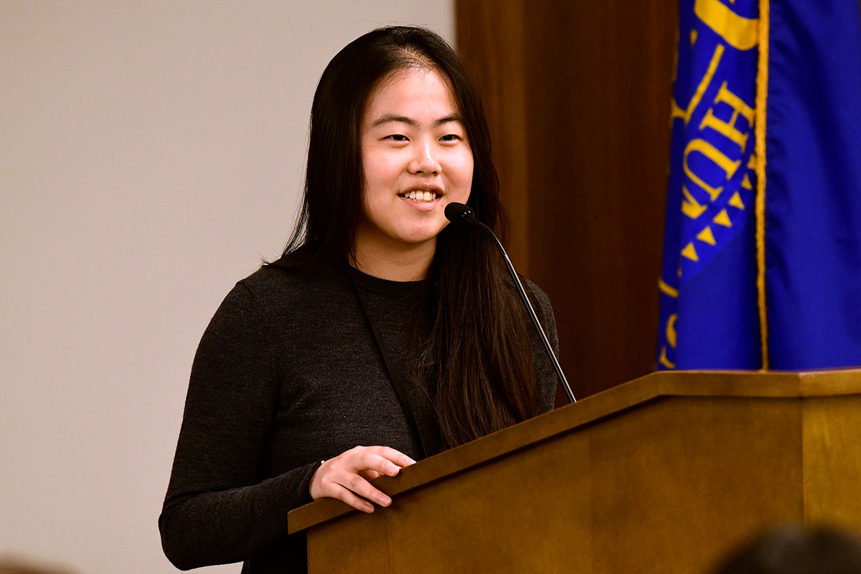 Sarah Feng stands before a microphone and podium