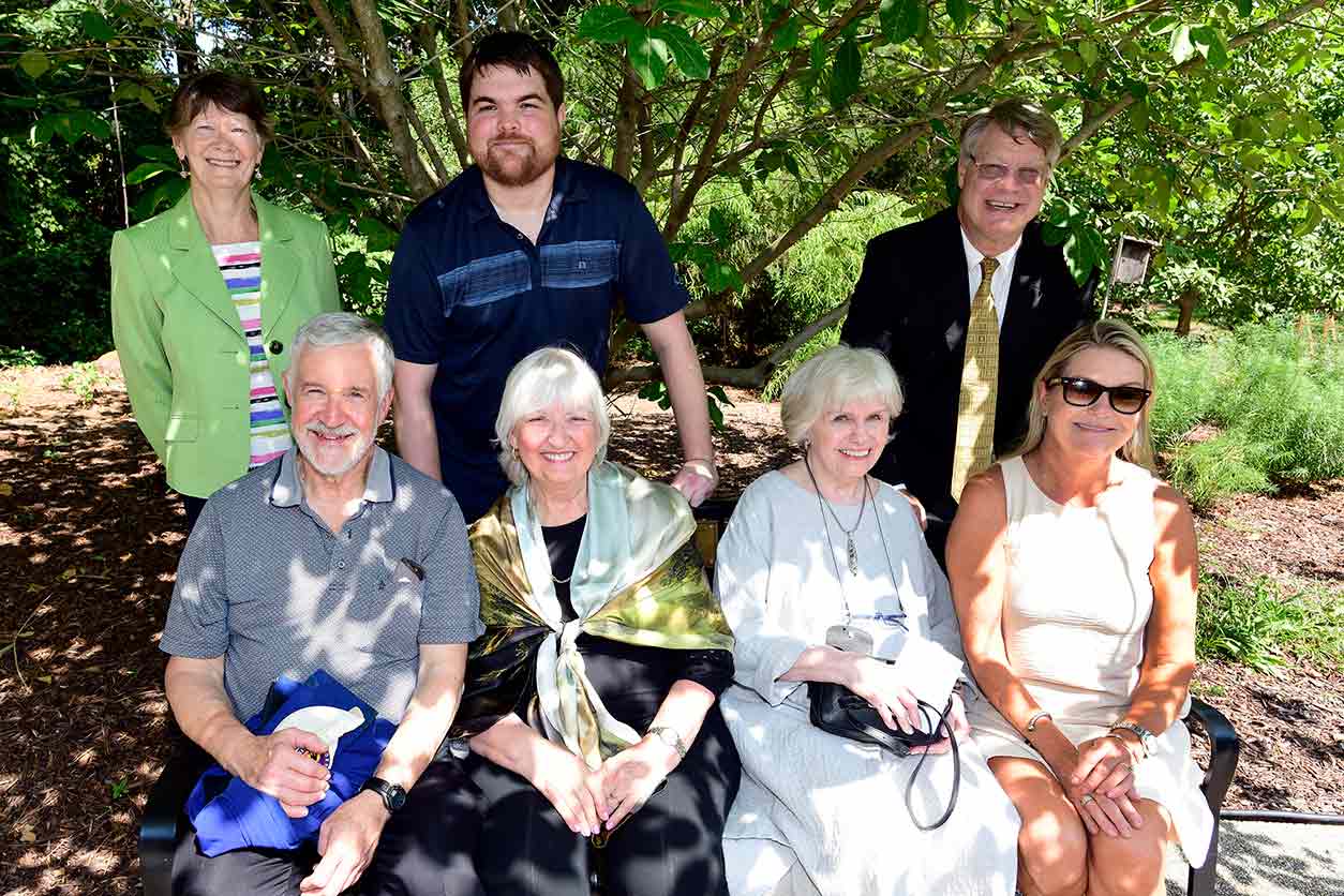 Wilson’s family and dearest friends posed for a photo on the newly dedicated bench. Back row, left to right: Rosemary Simpson (longtime friend, colleague), Brendan Kohler (grandson), and Van Houten. Front row: Joe Wilson (brother), Susan Wilson (sister-in-law), Dorothea Wilson (wife), and Kathy Kohler (daughter).