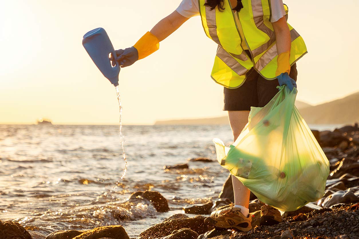 Person in yellow vest picking up plastic trash at beach