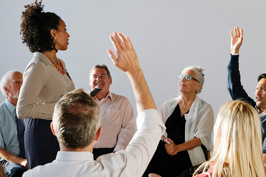 group of people sitting around a speaker. some people have their hands raised