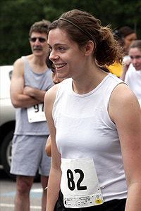 A smiling woman in running attire. Other runners are in the background.