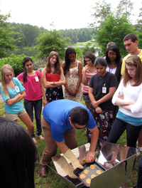 Shar Samy, Ph.D., uses a solar cook stove while students observe.
